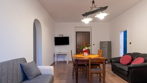 Un saló amb un sofà, una taula de dinar amb cadires, una televisió i un ventilador de sostre.