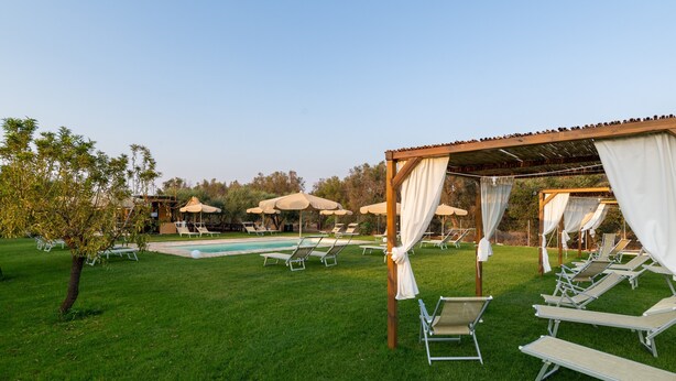 Zona de piscina amb gandules i ombrel·les, envoltada de vegetació.