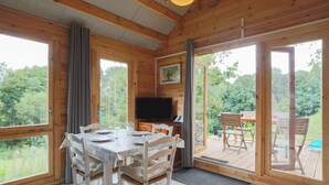 Interior de una cabaña de madera con una mesa de comedor, sillas, un televisor y vistas al exterior.
