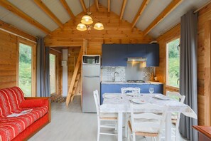 Interior de una cabaña de madera con una mesa de comedor para cuatro, una cocina con armarios azules y un sofá rojo.