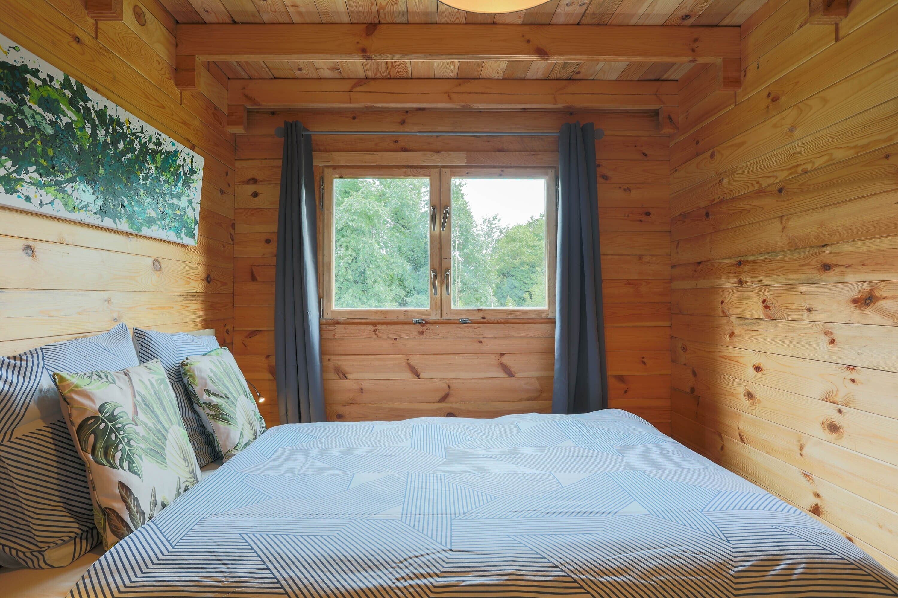 Una camera in legno con un letto, tende e una finestra.