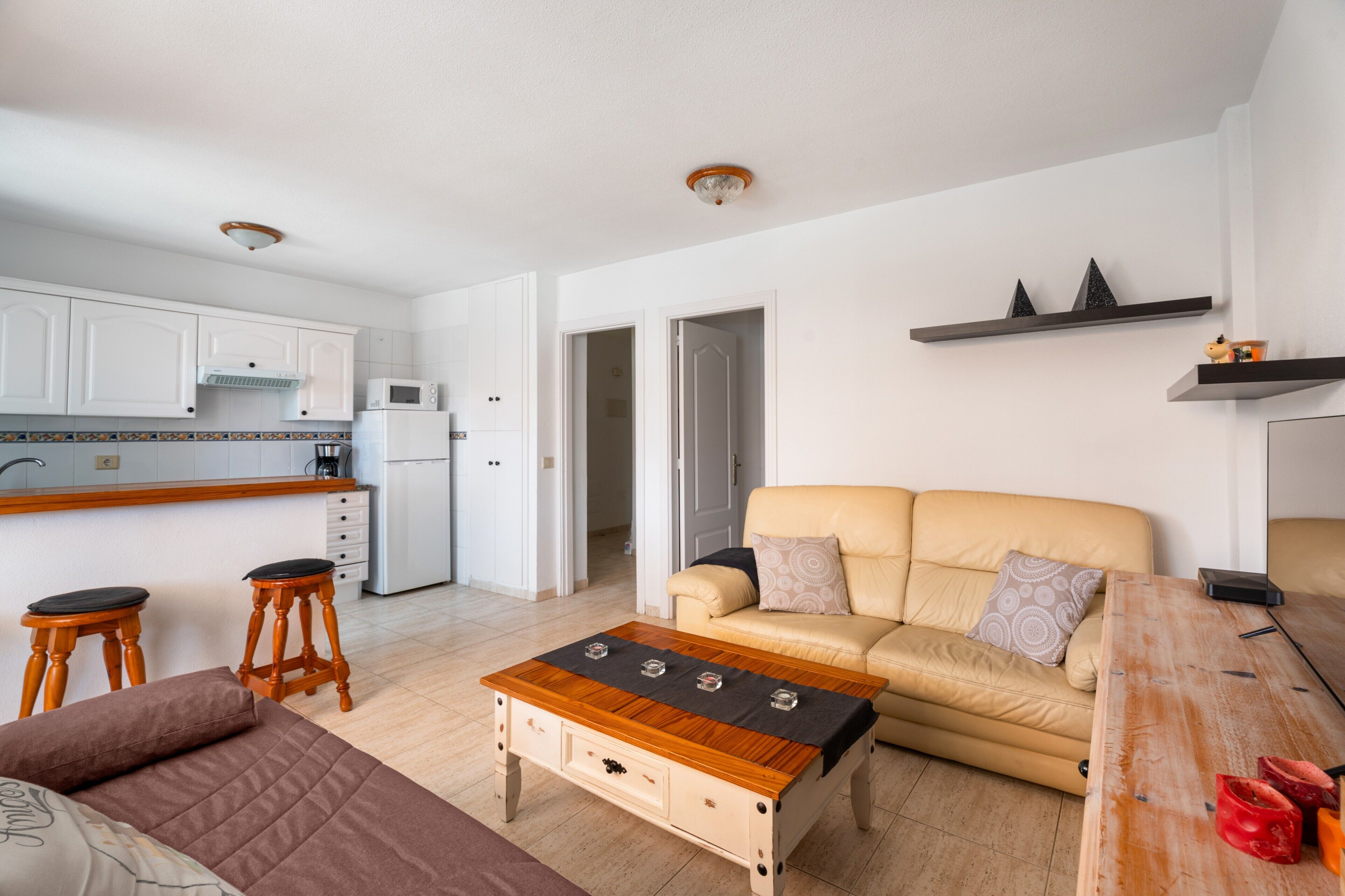A modern living space with a kitchen, a sofa, a coffee table, and a wooden dining table.