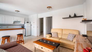 A modern living space with a kitchen, a sofa, a coffee table, and a wooden dining table.