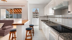 A modern kitchen with white cabinets, a black stove, and a window with a view of buildings. - Holiday Apartment 'Central Los Cristianos' with Mountain View, Pool and Wi-Fi (Los Cristianos)