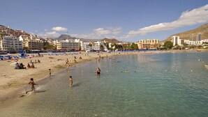 A beach with clear water, people swimming, and buildings in the background. - Holiday Apartment 'Central Los Cristianos' with Mountain View, Pool and Wi-Fi (Los Cristianos)