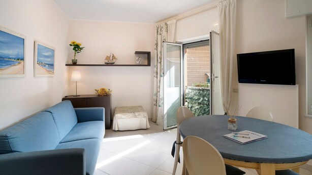 Un soggiorno moderno con un divano blu, un tavolo da pranzo con sedie, una TV a schermo piatto e un balcone con vista.