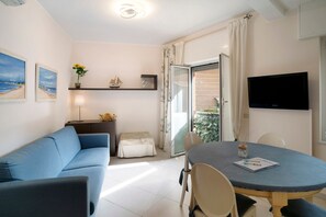 Un salon moderne avec un canapé bleu, une table à manger avec des chaises, un téléviseur à écran plat et un balcon avec vue.