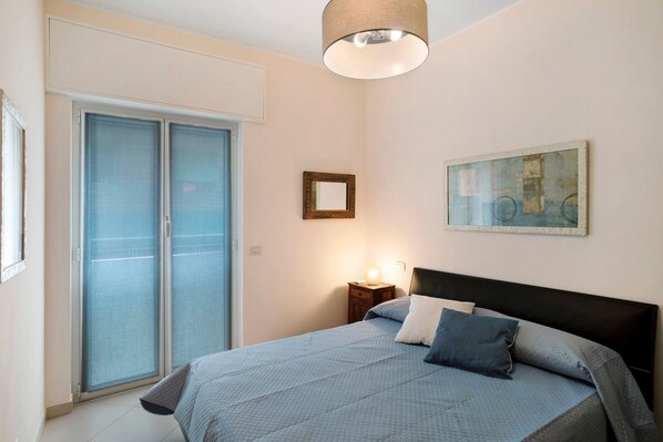 Une chambre à coucher comprenant un lit, une table de chevet, une lampe, un tableau encadré et une porte coulissante.
