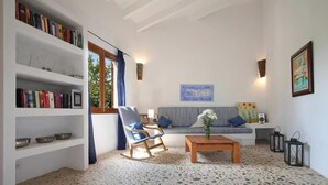 A living room with a sofa, a rocking chair, a coffee table, and a bookshelf. - Country House 'Finca Can Xanet' with Mountain Views, Wi-Fi and Air Conditioning (Alcúdia)