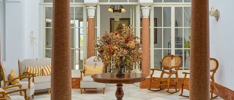 A room with a round wooden table, white upholstered chairs, and a large floral arrangement.