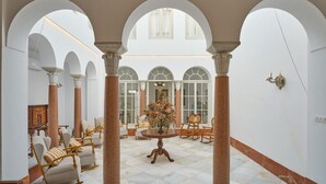 Ein weitläufiger Innenhof mit weißen Bögen, einem runden Tisch in der Mitte mit einer Blumenkomposition und Sitzbereichen mit Stühlen.