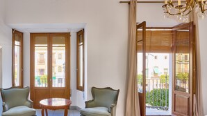Ein Zimmer mit zwei Stühlen, einem runden Tisch, einer Chandelier und Blick durch eine große Tür.