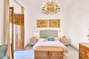 Een slaapkamer met een houten bed, twee nachtkastjes, een kroonluchter en twee florale schilderijen in lijsten aan de muur.