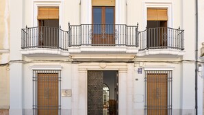 Ein Gebäude mit einem mittleren Eingang, zwei Balkonen mit schmiedeeisernen Geländern und einer großen Holztür mit Metallgitter.