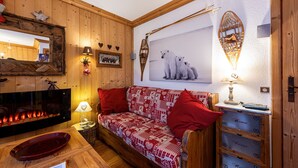 A cozy room with a wooden wall, a red and white patterned sofa, a fireplace, and a wall-mounted picture of polar bears. - Apartment 'Le Châtelard' with Mountain View, Private Terrace and Wi-Fi (Val-d'Isère)