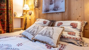 A bed with patterned pillows, a wall-mounted lamp, a framed picture, and a wooden wall. - Apartment 'Le Châtelard' with Mountain View, Private Terrace and Wi-Fi (Val-d'Isère)