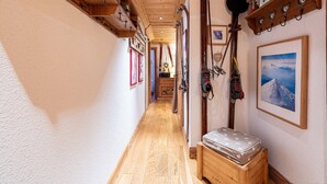 A narrow hallway with wooden flooring, a bench, and wall-mounted ski equipment. - Apartment 'Le Châtelard' with Mountain View, Private Terrace and Wi-Fi (Val-d'Isère)
