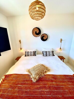 A bedroom with a large bed, two wall-mounted lamps, a woven ceiling light, and two woven wall decorations.