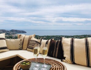 A terrace with a view of the sea, a wicker table with glasses and olives, and patterned cushions. - Holiday Home 'La Bohéme' with Sea View, Shared Pool and Wi-Fi (Teulada)