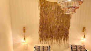 Een kamer met twee bedden, een klein houten krukje, een hangende geweven decoratie en twee wandlampen.