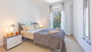 A bedroom with a bed, bedside tables, a nightstand, a window with curtains, and a view of palm trees. - Apartment 'Playa De Poniente' with Sea View, Wi-Fi and Air Conditioning (Benidorm)