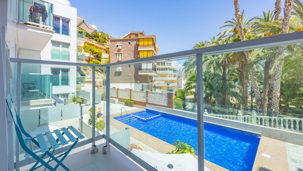 A balcony with a glass railing, a pool, and a view of neighboring buildings. - Apartment 'Playa De Poniente' with Sea View, Wi-Fi and Air Conditioning (Benidorm)