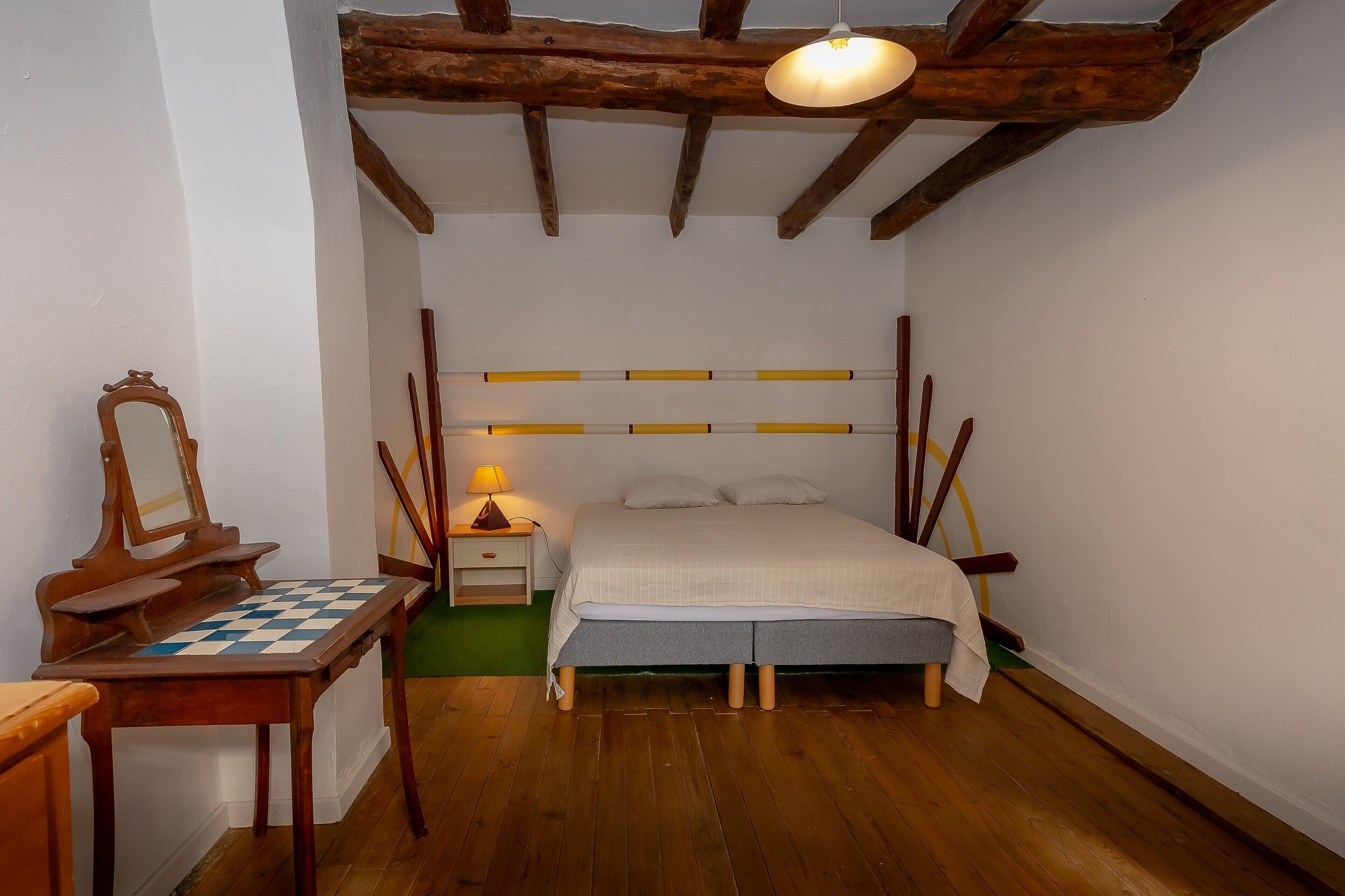 Une chambre à coucher avec un lit en bois, une table de chevet avec une lampe, une chaise en bois et un jeu d’échecs.