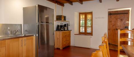 A kitchen with wooden cabinets, a stainless steel refrigerator, a wooden cabinet with appliances, a window, and a dining area with wooden chairs.