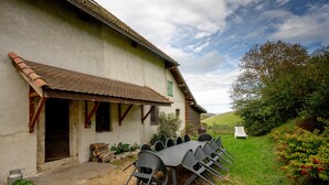 Ein rustikales Gebäude mit einem Essbereich, der einen langen Tisch und Stühle, eine Holztür und einen kleinen Garten mit einem Stuhl zeigt.