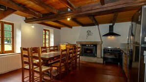 Ein Essbereich mit Holzkstühlen und einem Tisch, eine Küche mit Herd und Kühlschrank sowie ein Kamin.