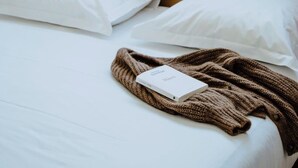 A bed with white sheets, two pillows, a brown knitted blanket, and a book titled 'Memoir.' - Holiday Home 'Gite Villa T1' with Shared Pool, Wi-Fi and Air Conditioning (Vals-les-Bains)