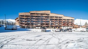 Een meerhoog hotel met balkons, een parkeerplaats en een besneeuwde omgeving.
