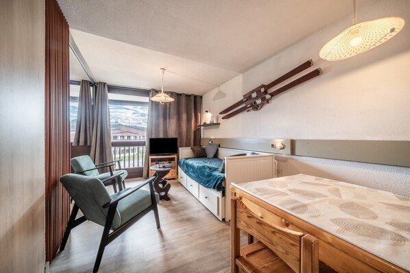 Une chambre moderne équipée d’un lit, d’un bureau, d’une chaise, d’une télévision et d’un balcon avec des rideaux.