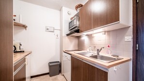 Een kleine keuken met houten kastjes, een magnetron, een vaatwasser en een spoelbak.