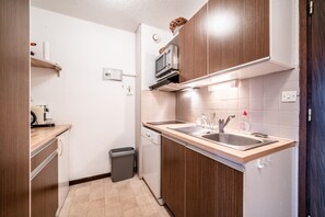 Una cocina compacta con armarios de madera, microondas, lavavajillas y un fregadero.