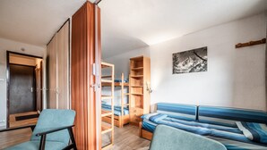 Een kamer met een stapelbed, een slaapbank, een stoel en een houten garderobe.