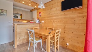 A wooden interior with a dining table, chairs, a microwave, and a TV mounted on the wall. - Apartment 'Appartement Alpe D'huez' with Balcony (Huez)