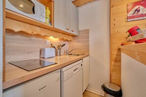 A kitchen with wooden cabinets, a dishwasher, a microwave, and a sink. - Apartment 'Appartement Alpe D'huez' with Balcony (Huez)
