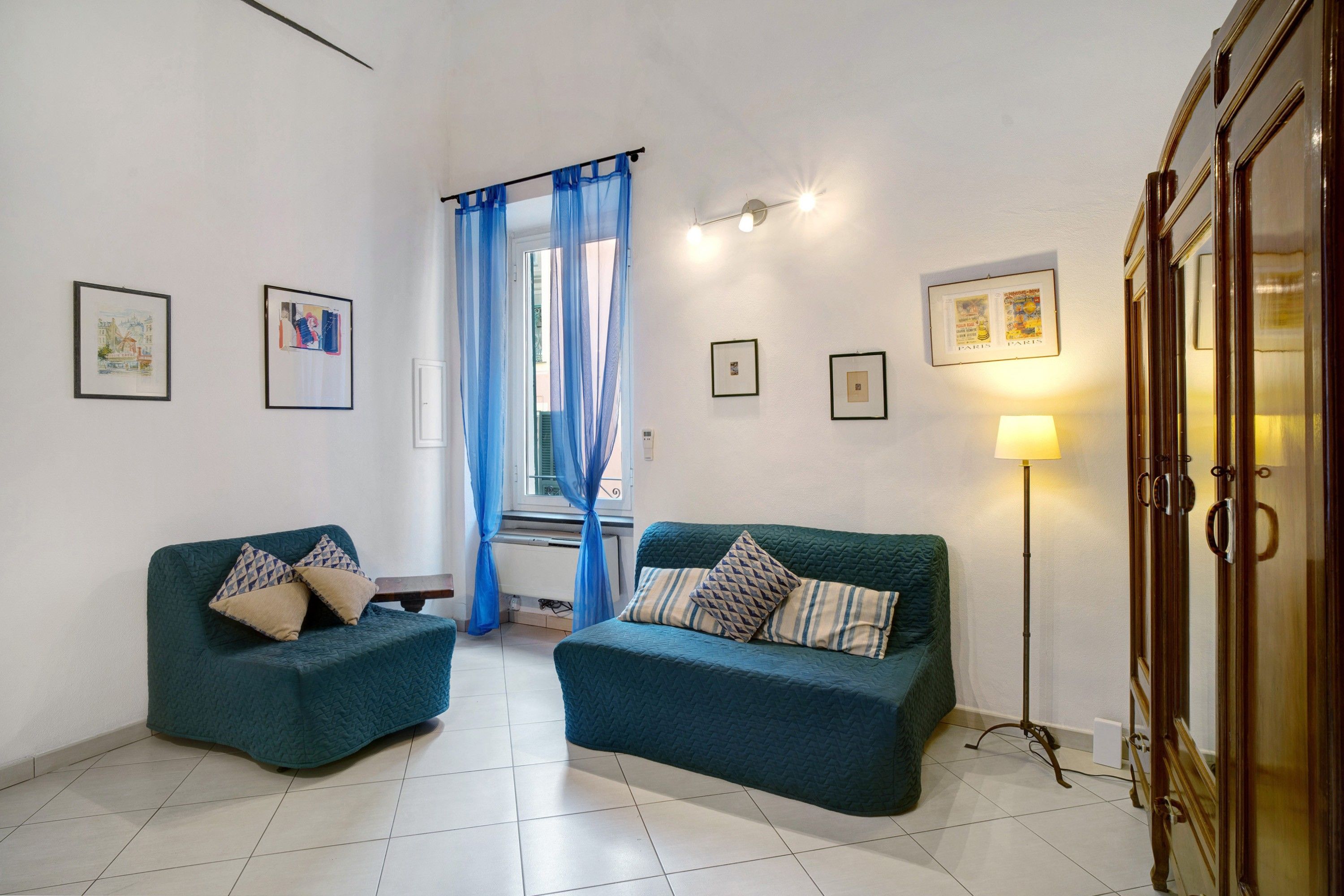 Ein Zimmer mit zwei türkisfarbenen Sofas, einer Stehlampe und gerahmten Bildern an den Wänden.