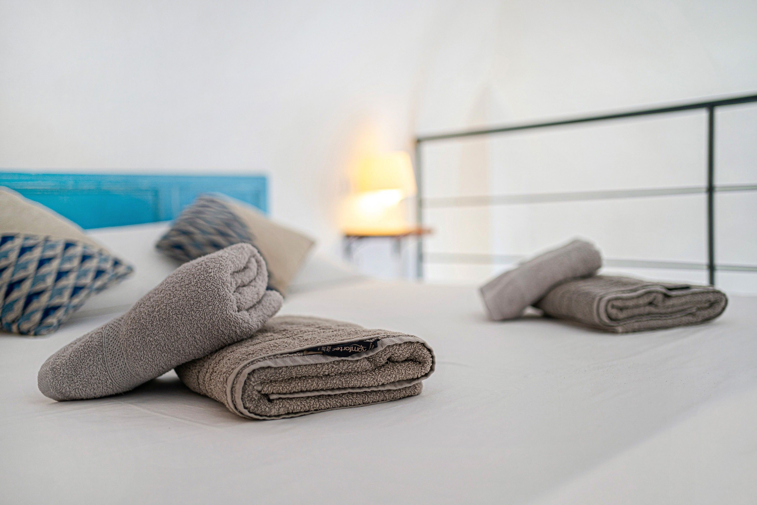 Un letto rifatto con asciugamani arrotolati e una lampada sullo sfondo.