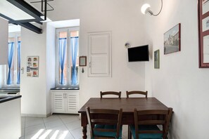 Un comedor con una mesa y sillas de madera, una ventana con cortinas, un televisor montado en la pared y un ventanal con vistas al exterior.