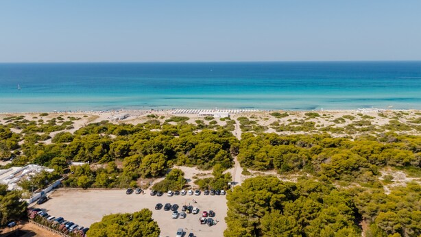 Vue aérienne d’une zone côtière avec une plage, un parking et une végétation luxuriante.