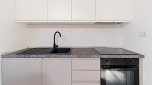 Une cuisine équipée d’un évier, d’une cuisinière, d’un four et de meubles de rangement blancs.