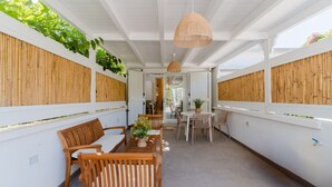 Un espace extérieur abrité, aménagé avec du mobilier en bois, un luminaire suspendu et des plantes grimpantes.