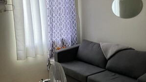 Ett vardagsrum med en grå soffa, en rund spegel på väggen och en golvfläkt.