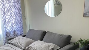 Ett modernt sovrum med en säng, en grå soffa och ett litet sidobord med en växt.