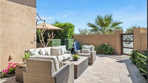 Un patio al aire libre con mobiliario de mimbre, una mesa baja y una zona de estar cubierta.