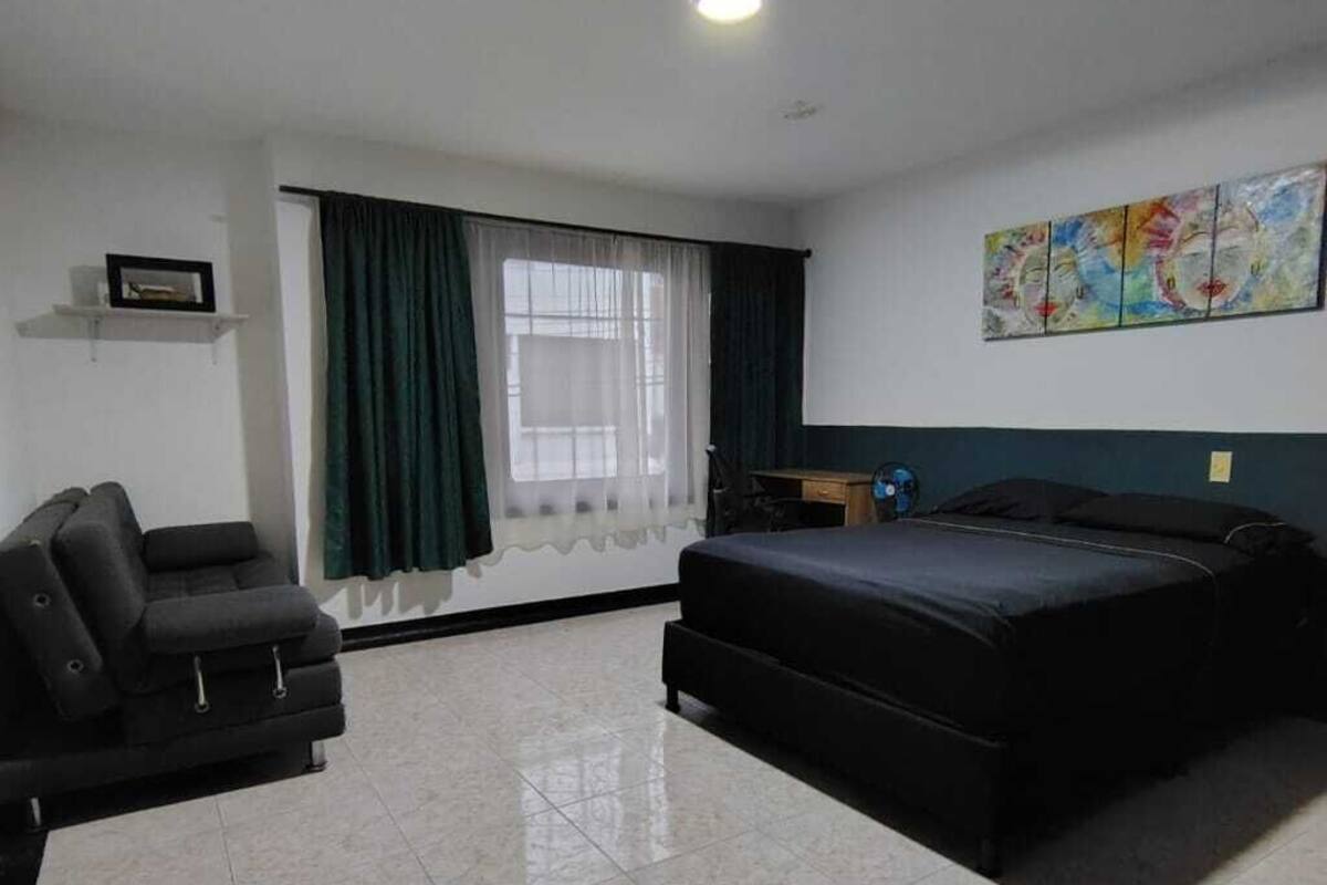 Una habitación de hotel con cama, sofá, escritorio y ventana con cortinas.