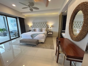 Una habitación de hotel moderna con una cama grande, un ventilador de techo, una mesita de madera y un espejo amplio.