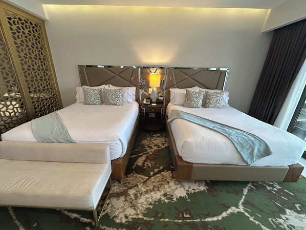 Habitación de hotel con dos camas, una mesita de noche, una lámpara y un panel decorativo en la pared.